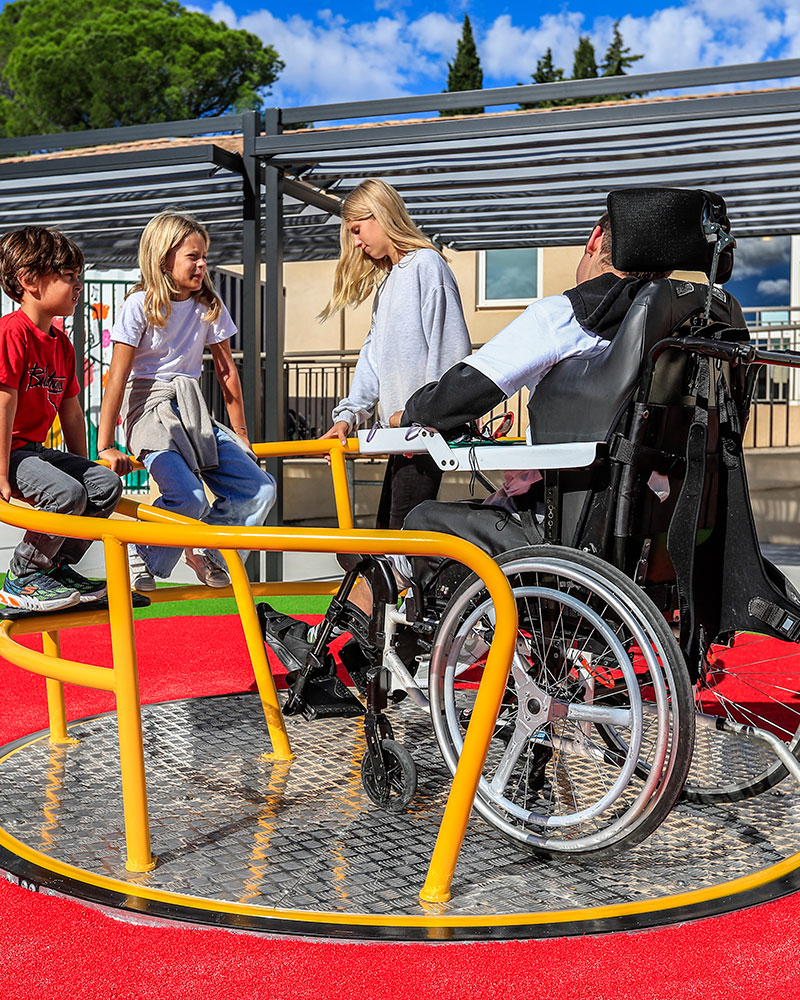 Un gruppo di bambini, tra cui una persona in sedia a rotelle, gioca insieme su una rotonda accessibile e inclusiva.